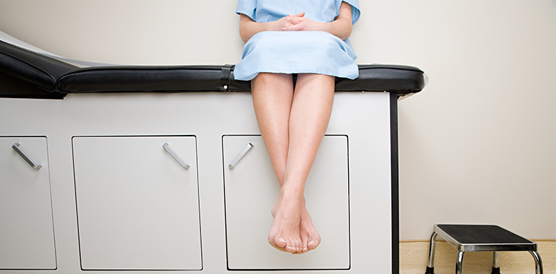 Woman wearing hospital gown sitting on examination table