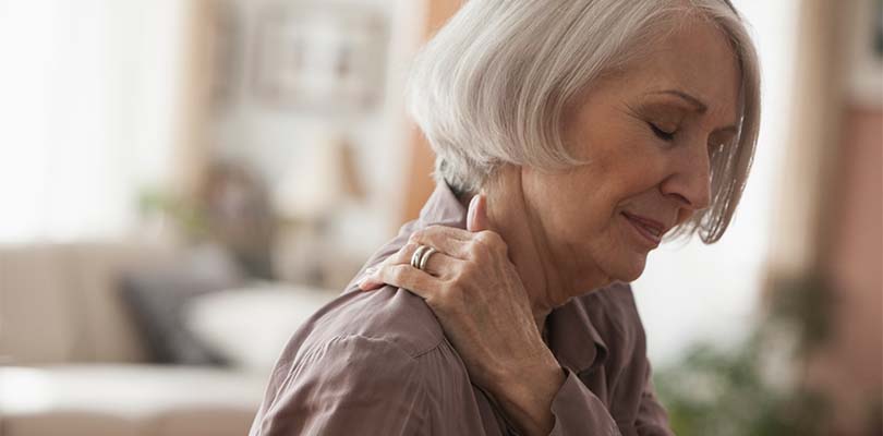 An elderly women holding her shoulder.